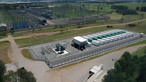 Aerial view of a battery storage facility with green and white containers beside a large electricity substation